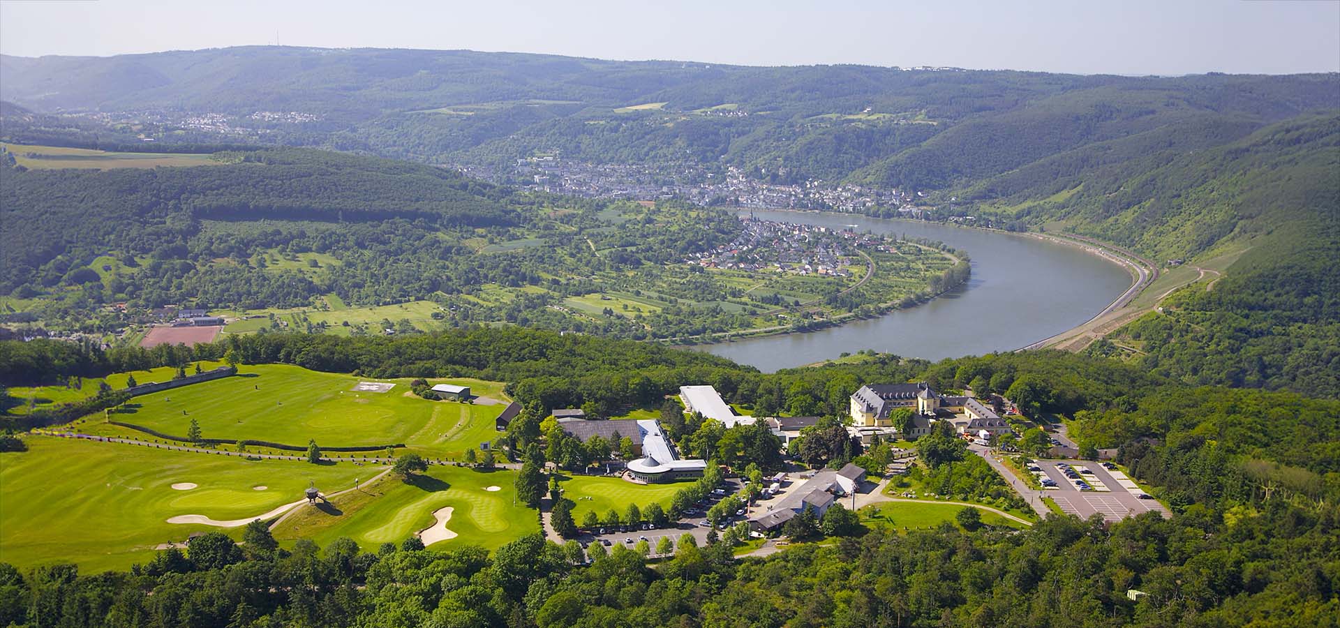 Ansicht des Hotel Jakobsberg von oben und mit Flussbett, Bergen und Stadt im Hintergrund