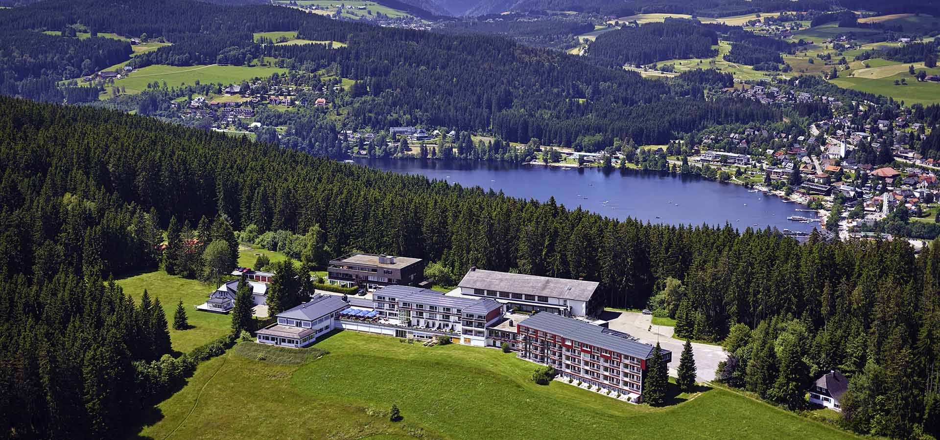 Ansicht des Hotel Sagerhöh von oben und von einem See, Bergen und einer Stadt im Hintergrund