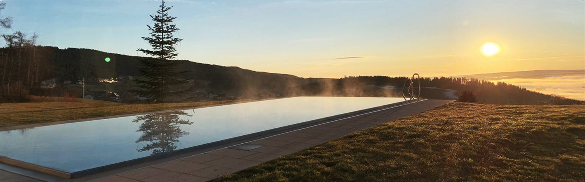 Ansicht des Außenbereichs mit Pool vom Hotel Sagerhöh und einem Sonnenuntergang im Hintergrund