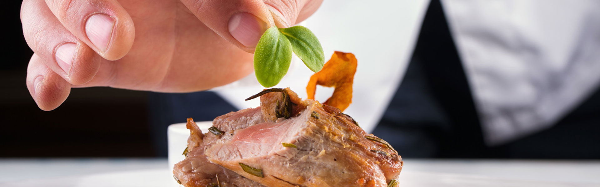 Ansicht auf ein gebratenes Fleischfilet und eine Hand, die eine Kresse-Garnitur darauf setzt