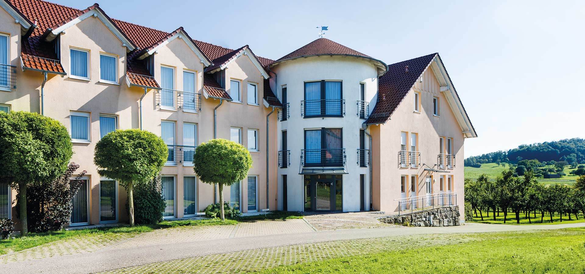 Außenansicht auf das Landhotel Beck und im Hintergrund ist eine Baumplantage und ein Berg