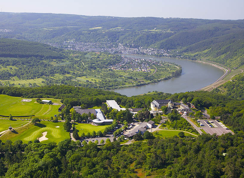 Ansicht des Hotel Jakobsberg von oben und mit Flussbett, Bergen und Stadt im Hintergrund