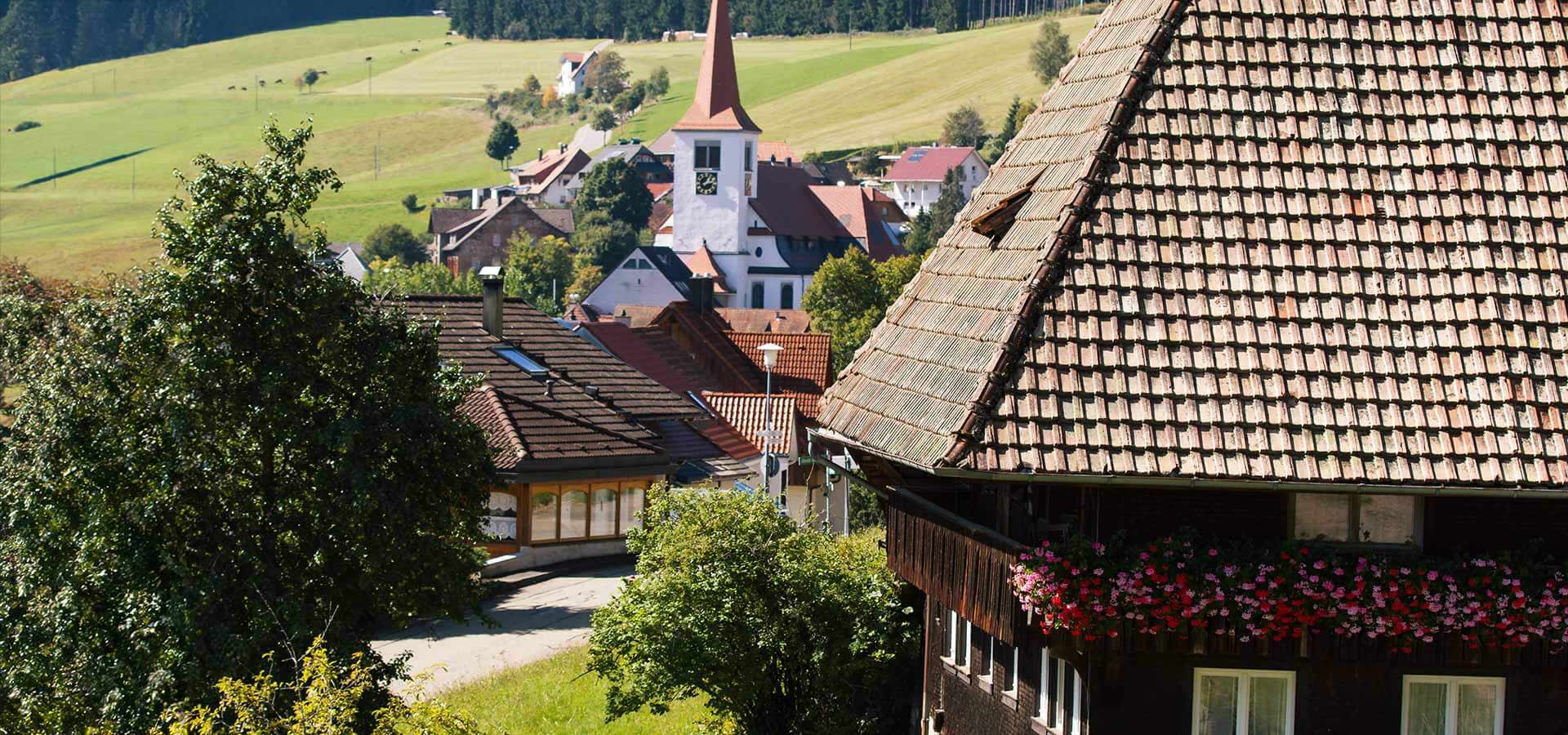 Außenansicht auf das Landhotel Rebstock mit Schwarzwaldhaus davor und Dorfkirche dahinter